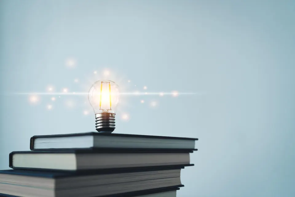 Light bulb on stacked books representing business innovation, leadership development, strategic thinking, and continuous learning.